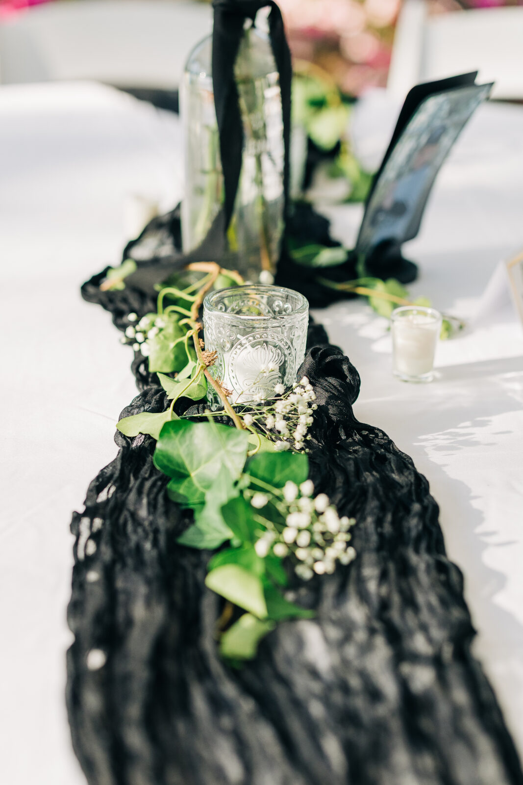 Detail of a reception table runner made of textured black gauze, decorated with sprigs of ivy, baby's breath, and a clear glass votive candle at the Hartley House Wedding South Carolina reception