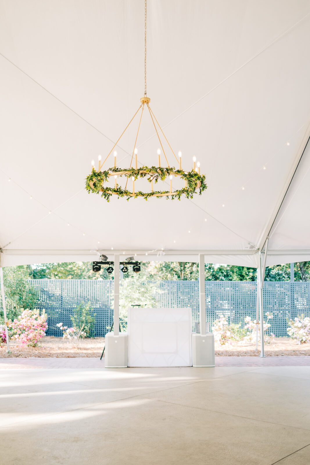 Wide shot of the white open-sided reception tent showing the dance floor, a white DJ booth, and a large gold chandelier decorated with greenery hanging from the ceiling at the Hartley House Wedding South Carolina
