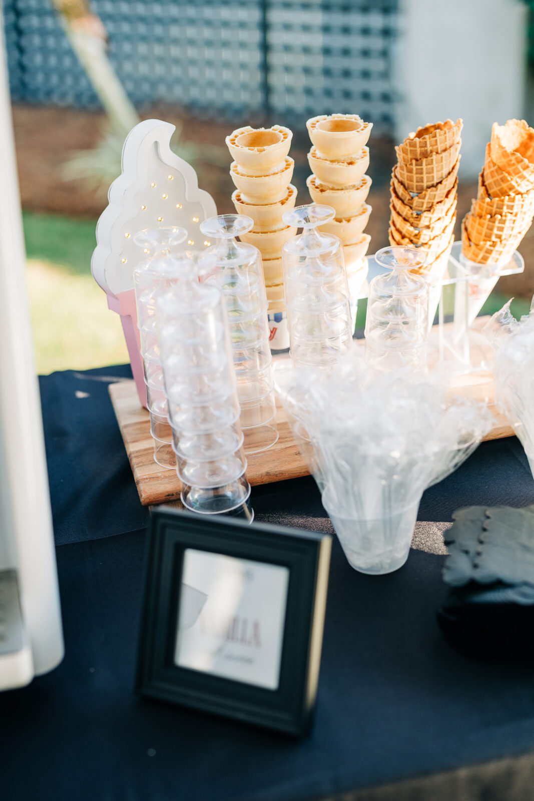 Close-up of the dessert bar with stacks of sugar cones and waffle cones, clear plastic cups, and a neon ice cream sign for the soft-serve station at the Hartley House Wedding South Carolina