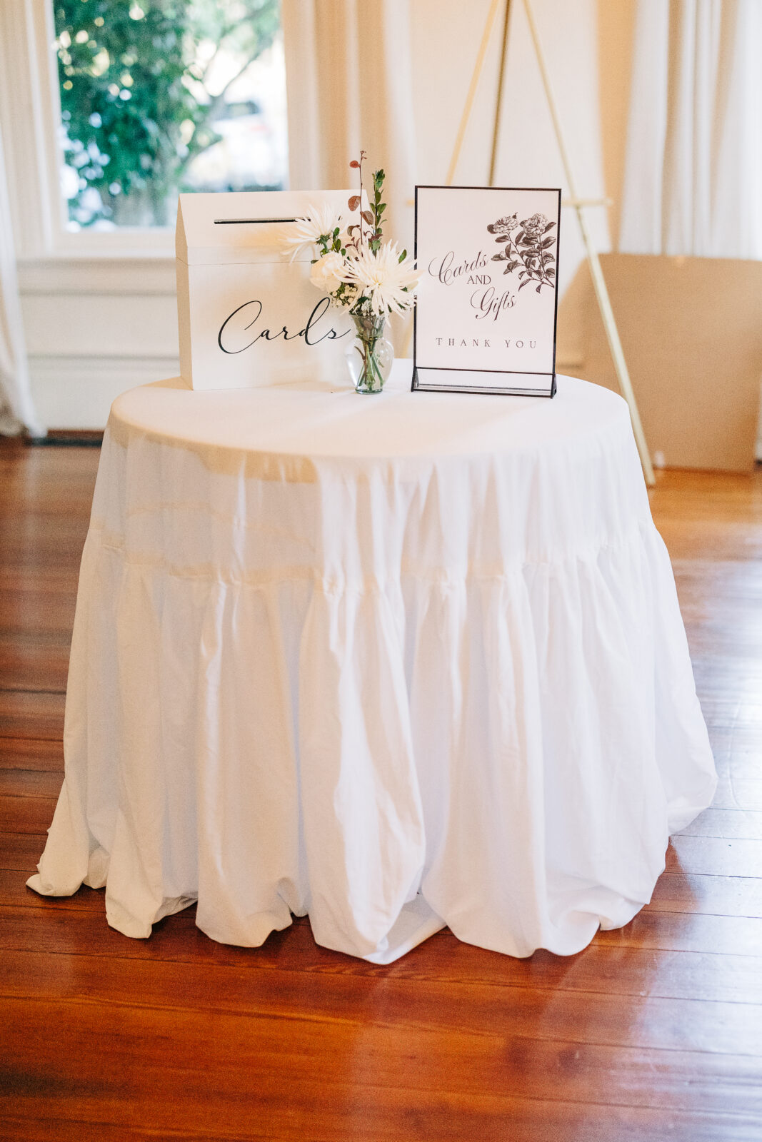 The "Cards and Gifts" table, featuring a small white ruffled linen, a simple floral centerpiece, a card box, and a framed sign, set up inside the Hartley House