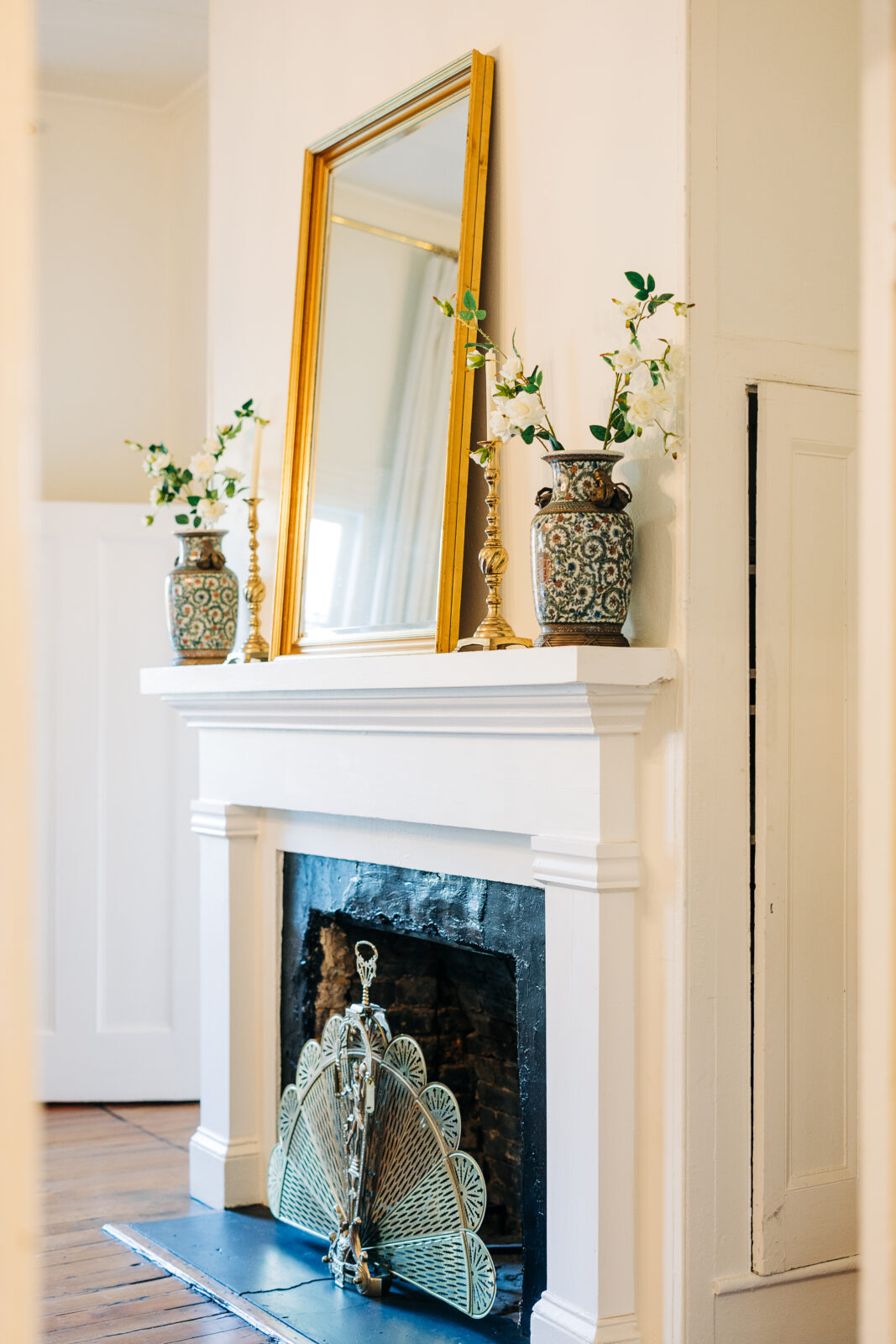 Interior detail of the venue showing a white fireplace mantle decorated with two ornate vases of flowers, gold candlesticks, and a large gold mirror above, reflecting the elegant style of the Hartley House Wedding South Carolina