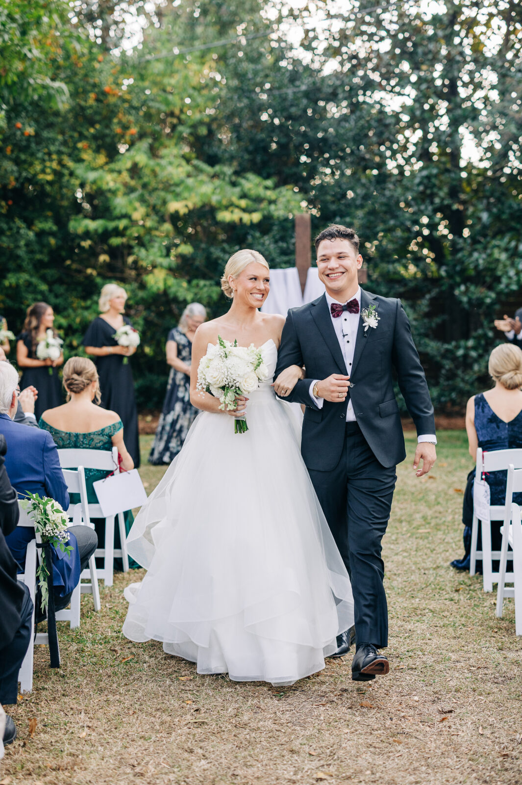 The newly married couple smiles brightly as they walk back up the aisle holding hands after their ceremony at the Hartley House Wedding South Carolina, cheered by guests