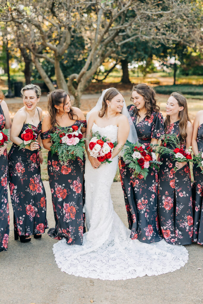 Bride surrounded by bridesmaids holding red and white bouquets during a multicultural wedding celebration.