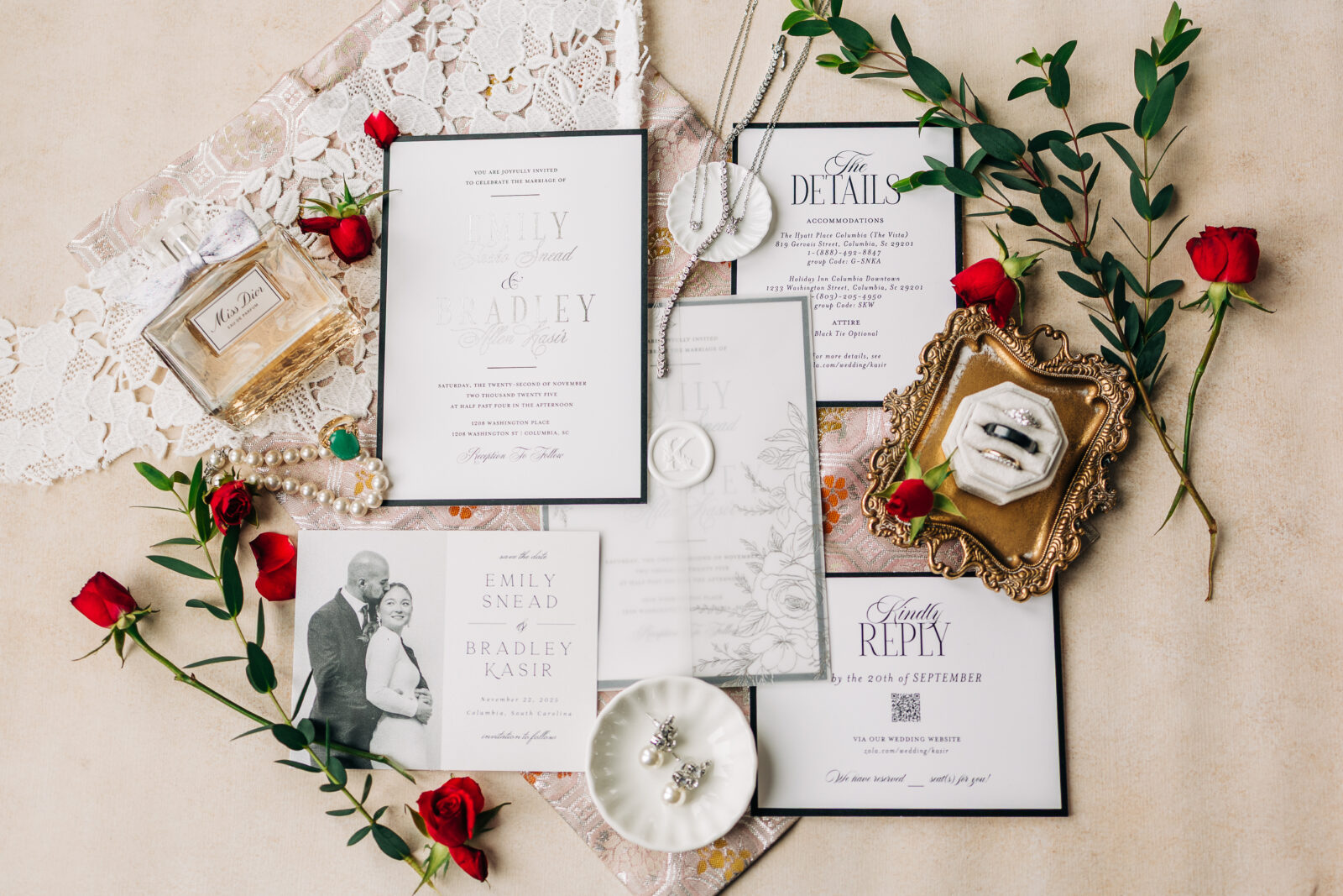 Flatlay of Emily and Bradley’s wedding invitation suite with red roses and jewelry for their 1208 Washington Place celebration.