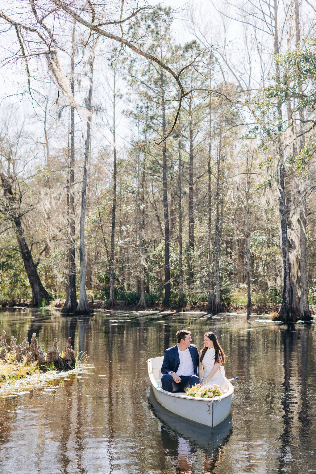 Peaceful engagement photo at Cypress Gardens with couple sitting in a rowboat framed by tall cypress trees.