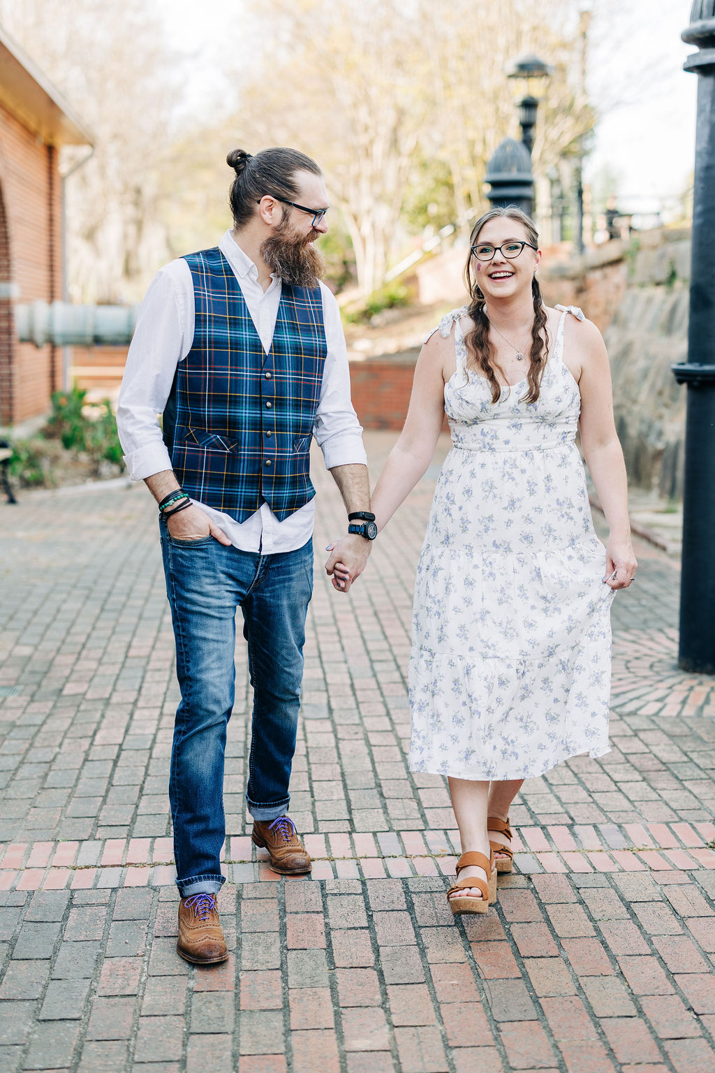 Couple holding hands and walking along a brick pathway during a downtown engagement session