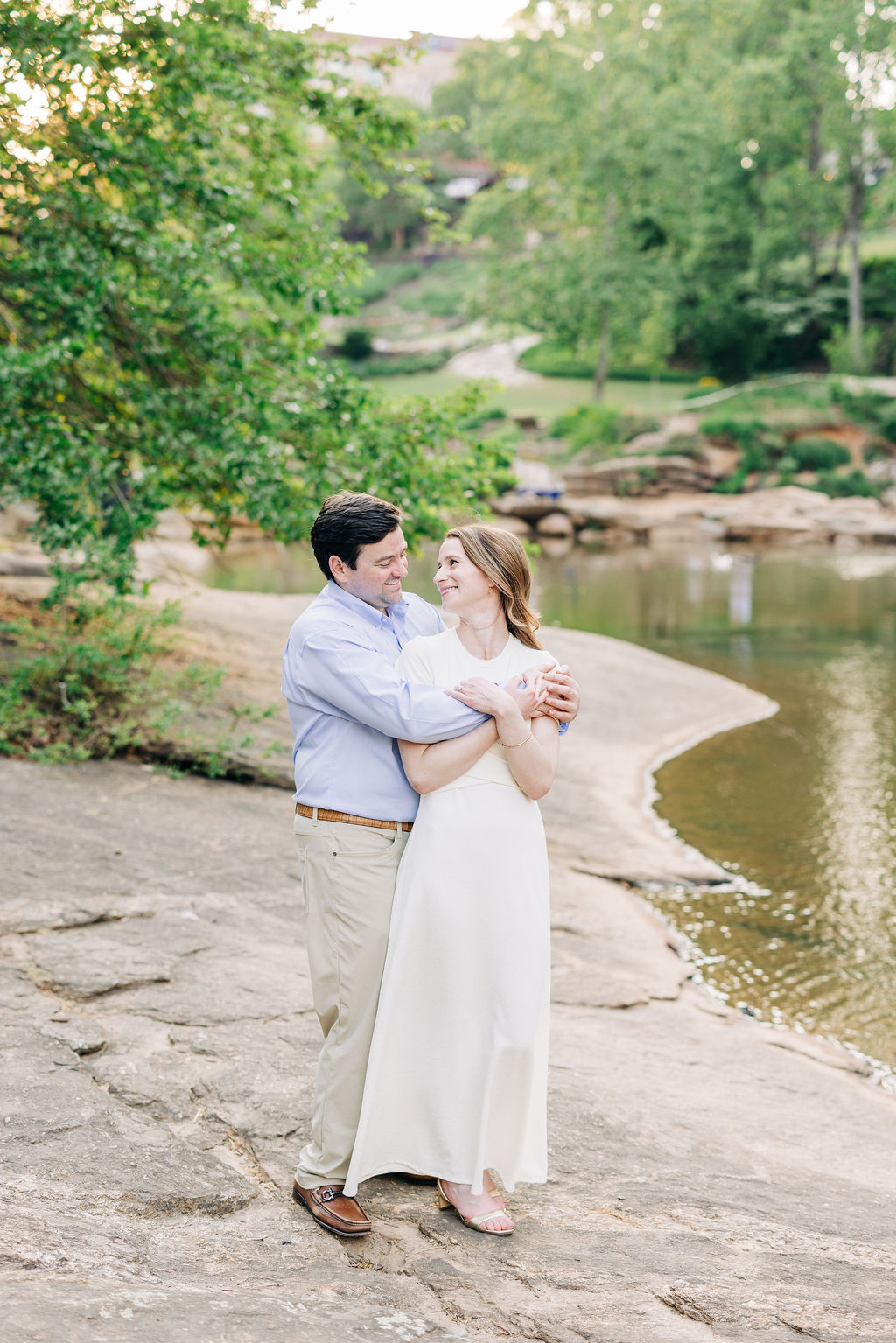 Romantic engagement session by the river with a couple embracing along a scenic shoreline
