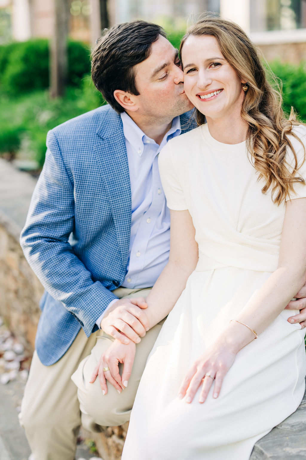 Close-up engagement photo of a couple smiling as one kisses the other on the cheek outdoors