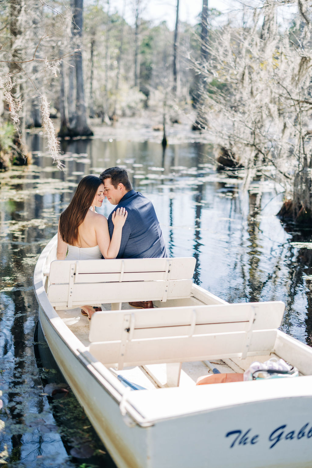 Romantic Cypress Gardens engagement photo of couple seated together in a small boat surrounded by cypress trees.