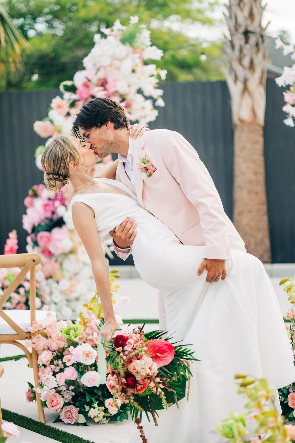 Couple standing together beneath a floral ceremony installation, foreheads touching