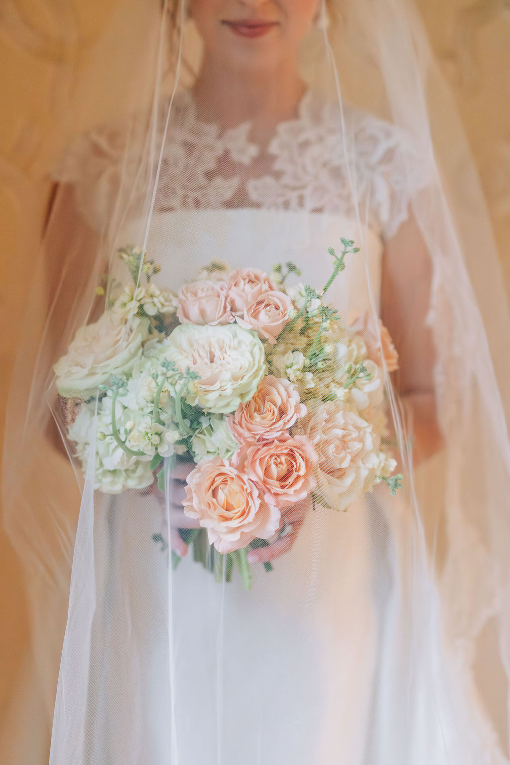 Bride holding her bouquet beneath a sheer veil creating a soft, romantic detail shot