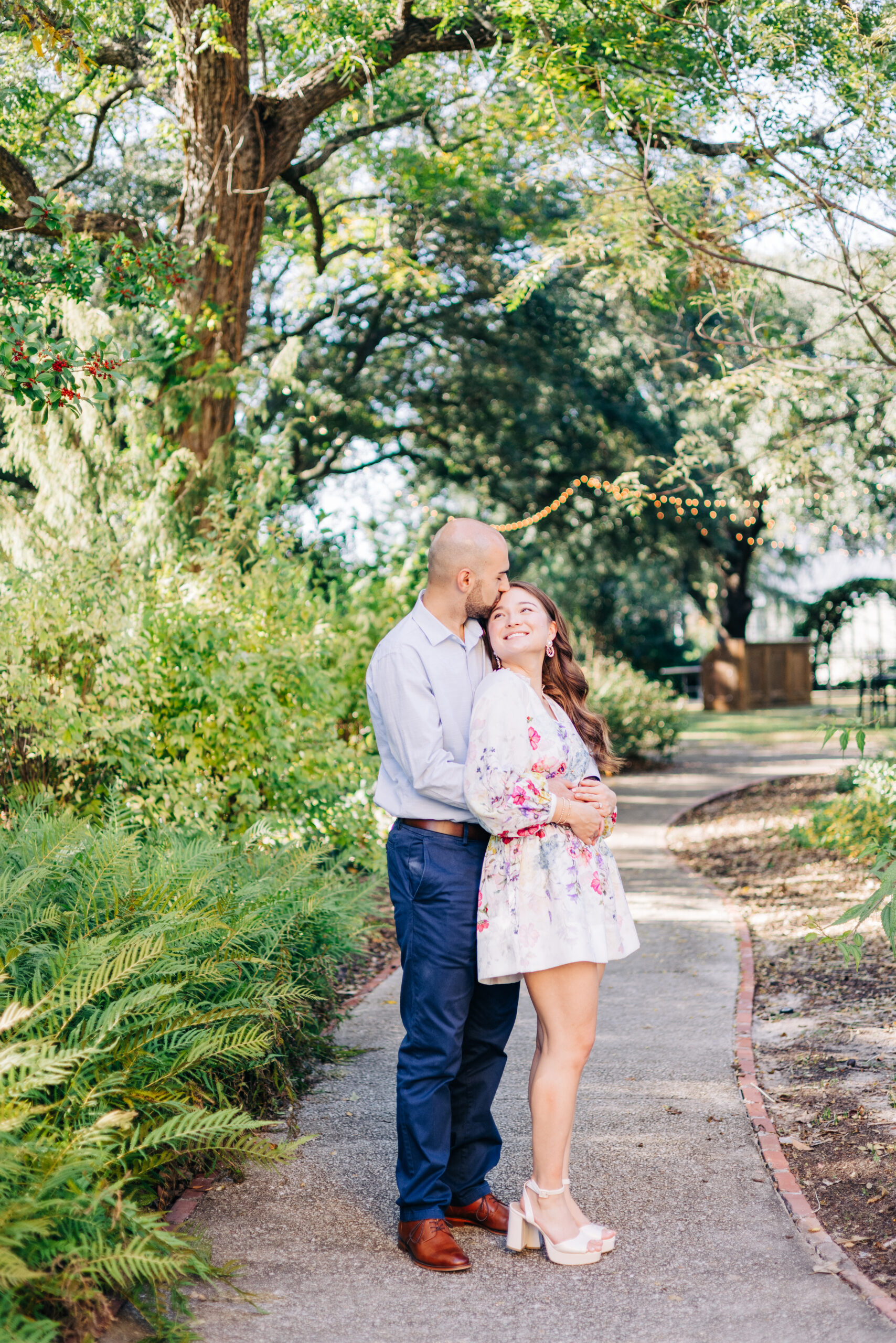 Man standing behind his partner and hugging her as she smiles on a tree lined walkway
