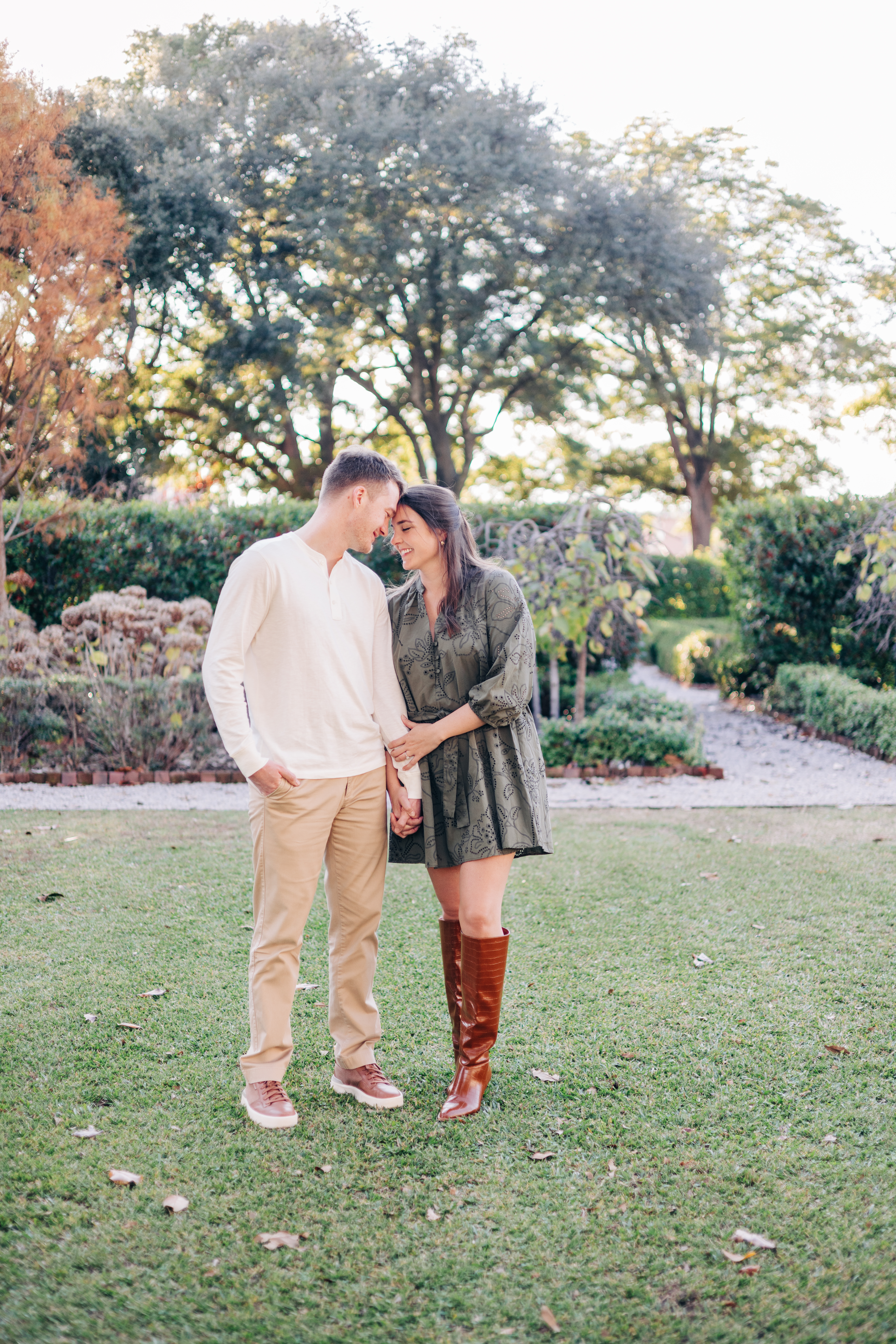 Couple standing close together on the grass, smiling softly at each other